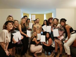 A group of smiling women on a hen party surround a smiling but nude male life model.