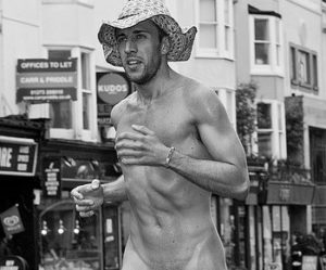 Hens with Pens life model Lorenzo running along a street nude, wearing only a straw hat